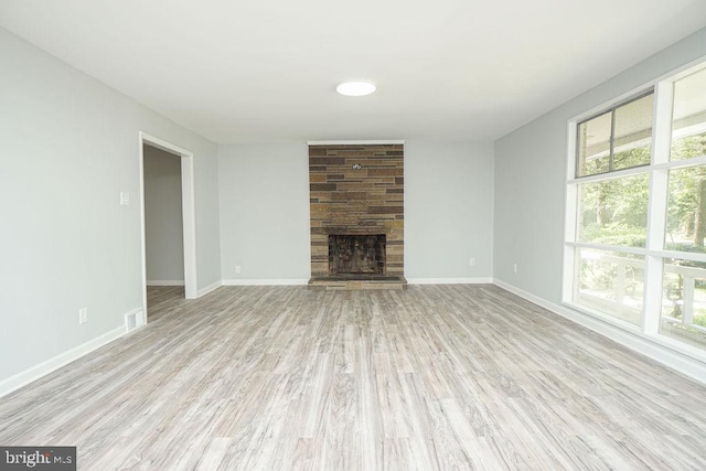 unfurnished living room with baseboards, visible vents, wood finished floors, and a stone fireplace