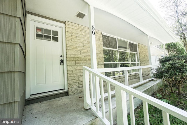 doorway to property with covered porch and brick siding