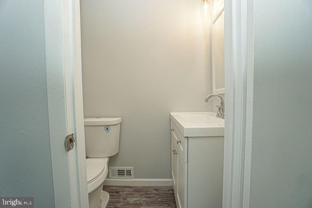 half bath with visible vents, toilet, vanity, wood finished floors, and baseboards