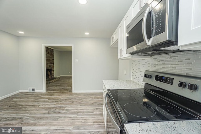 kitchen featuring baseboards, white cabinets, decorative backsplash, appliances with stainless steel finishes, and light wood-type flooring