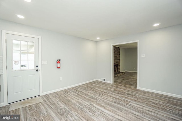 foyer featuring a fireplace with raised hearth, wood finished floors, and recessed lighting