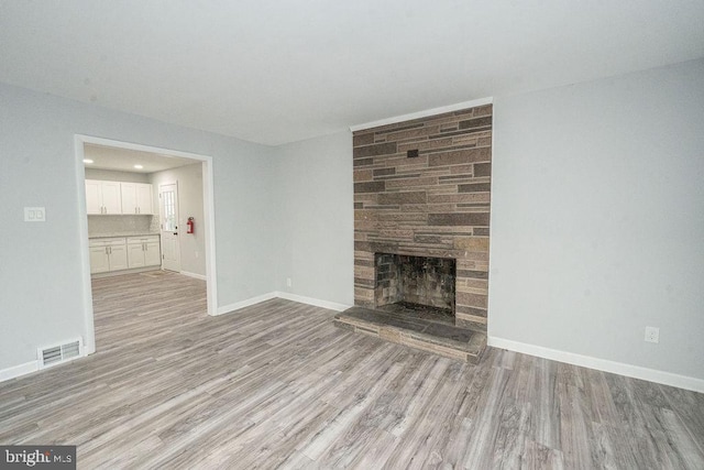 unfurnished living room with baseboards, visible vents, a stone fireplace, and light wood finished floors