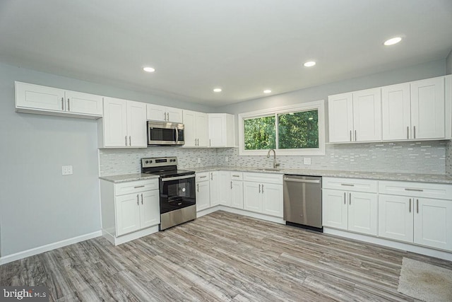 kitchen with light stone counters, stainless steel appliances, a sink, white cabinetry, and light wood-type flooring