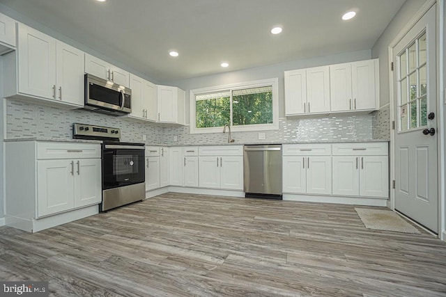 kitchen featuring light stone counters, stainless steel appliances, white cabinetry, light wood-style floors, and backsplash