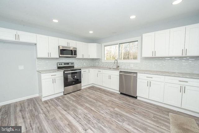 kitchen featuring light wood finished floors, decorative backsplash, white cabinets, appliances with stainless steel finishes, and a sink