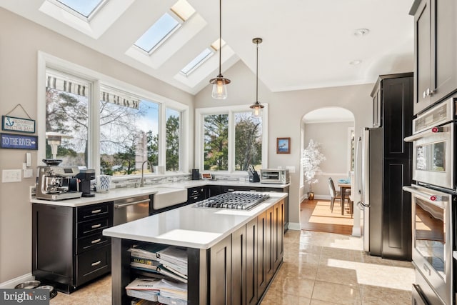 kitchen with lofted ceiling, arched walkways, a sink, stainless steel appliances, and light countertops