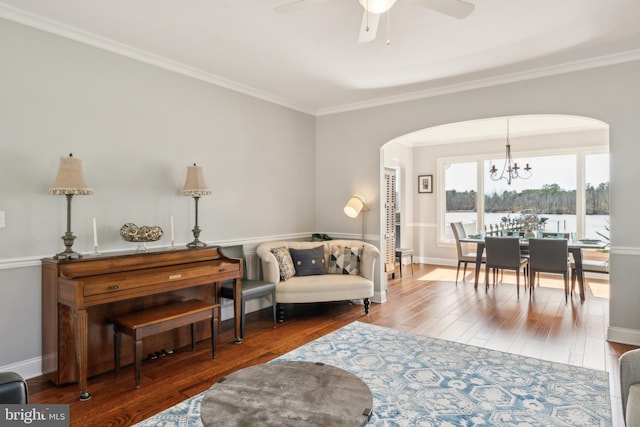 living area featuring baseboards, arched walkways, wood finished floors, and crown molding