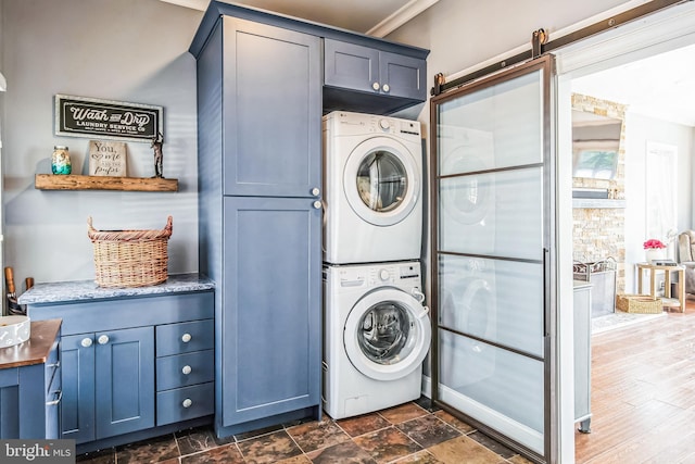 laundry room featuring a barn door, cabinet space, stacked washer and clothes dryer, and stone finish flooring