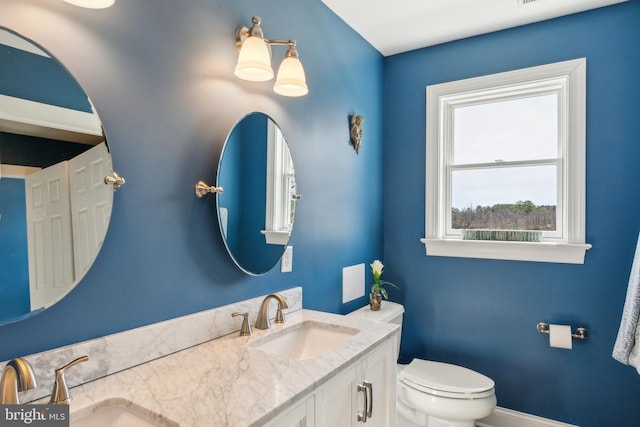 bathroom featuring double vanity, toilet, baseboards, and a sink