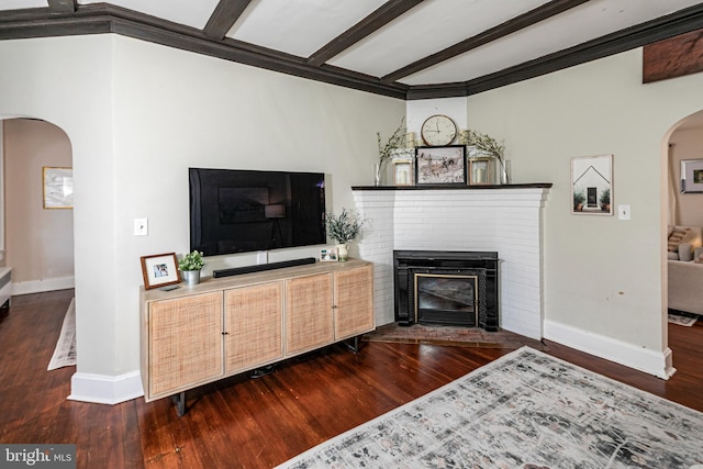 living room featuring beamed ceiling, arched walkways, a brick fireplace, and wood finished floors