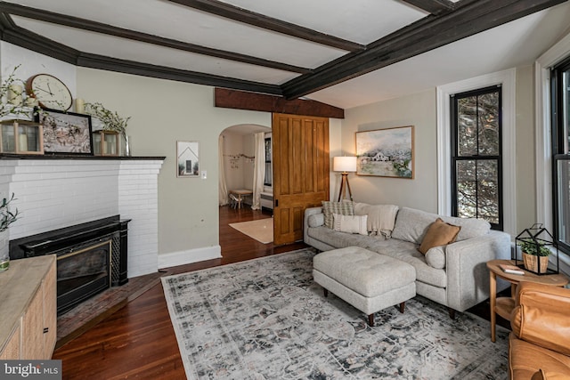 living room with dark wood-style floors, baseboards, beam ceiling, arched walkways, and a brick fireplace