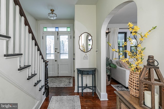 foyer entrance with stairway, arched walkways, baseboards, and dark wood finished floors