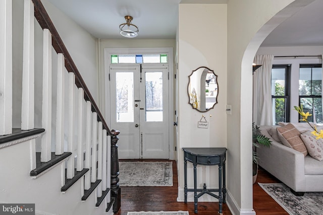 entrance foyer featuring baseboards, arched walkways, dark wood finished floors, and stairs