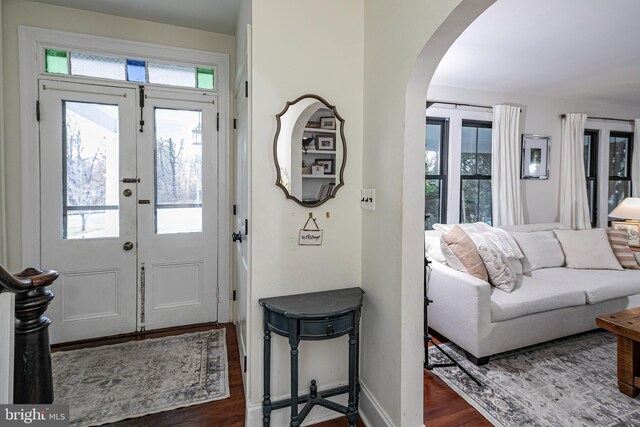 foyer entrance featuring dark wood-type flooring, baseboards, and arched walkways