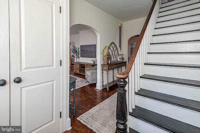 staircase featuring arched walkways and wood finished floors