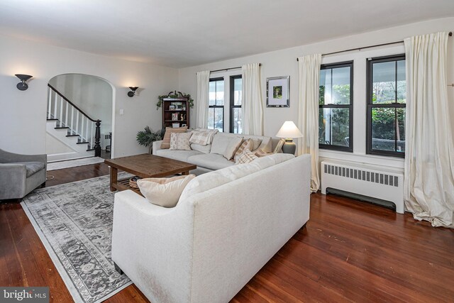 living room featuring arched walkways, radiator, dark wood finished floors, and stairs