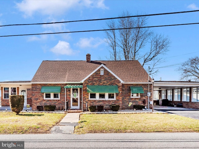 view of front of home featuring a chimney, a front lawn, a carport, and brick siding