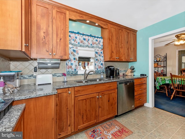 kitchen with dishwasher, brown cabinetry, dark stone counters, and a sink