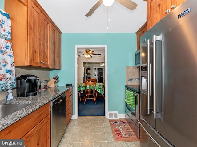 kitchen featuring brown cabinets, tasteful backsplash, visible vents, appliances with stainless steel finishes, and dark stone counters