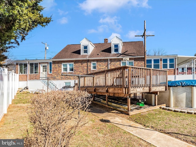 back of property with a lawn, roof with shingles, fence, a wooden deck, and brick siding