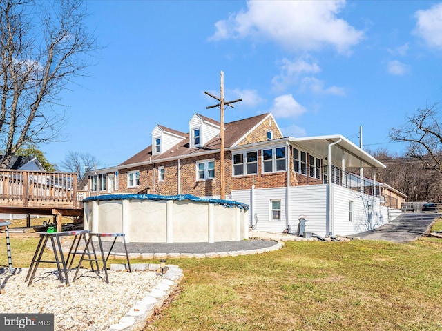 back of house featuring a yard, brick siding, and a covered pool