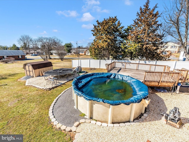 view of swimming pool with a lawn, a covered pool, a fenced backyard, a trampoline, and a deck