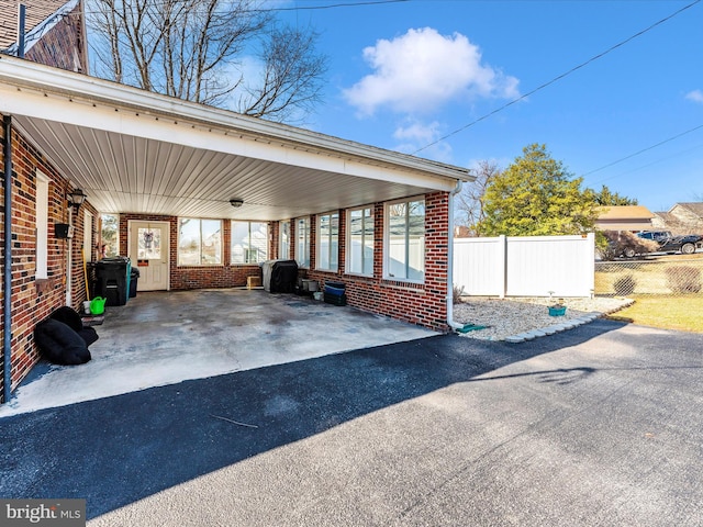 view of vehicle parking with a carport, aphalt driveway, and fence