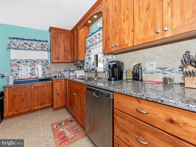 kitchen with decorative backsplash, stainless steel dishwasher, brown cabinetry, a sink, and dark stone countertops