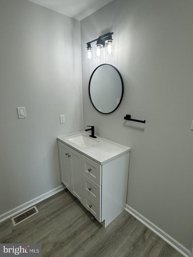 bathroom with visible vents, vanity, baseboards, and wood finished floors