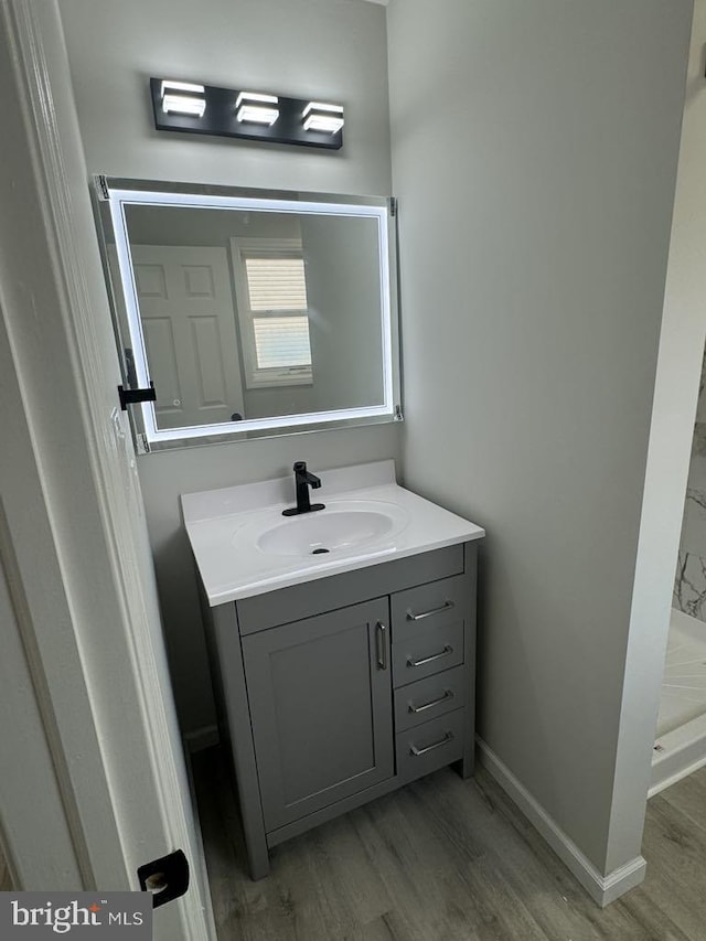 bathroom featuring walk in shower, wood finished floors, vanity, and baseboards