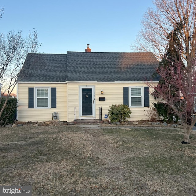 view of front facade featuring a front yard, roof with shingles, and a chimney