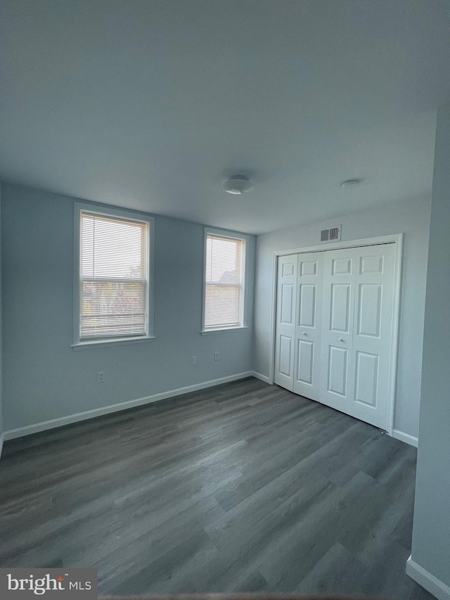 unfurnished bedroom with dark wood-style floors, a closet, visible vents, and baseboards