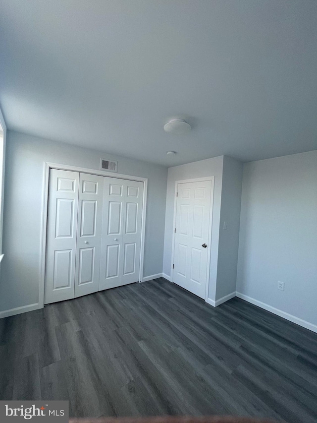 unfurnished bedroom featuring baseboards, a closet, visible vents, and dark wood-type flooring