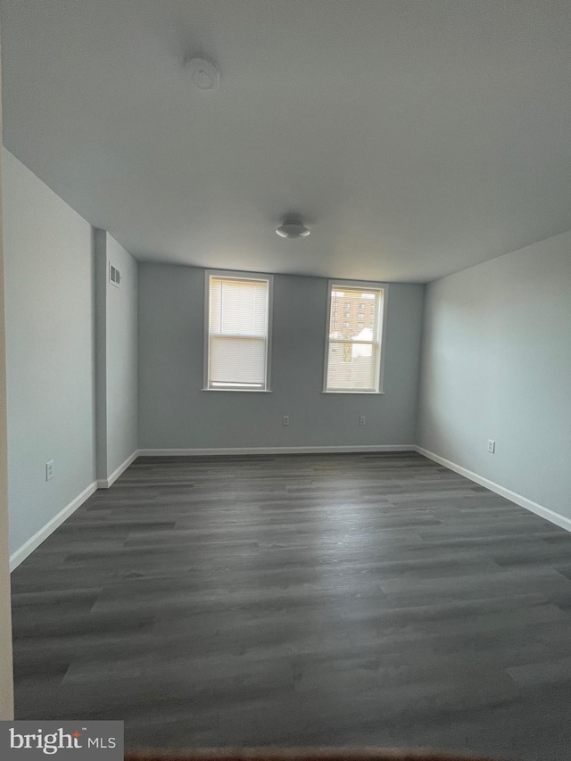 empty room with dark wood-style flooring, visible vents, and baseboards