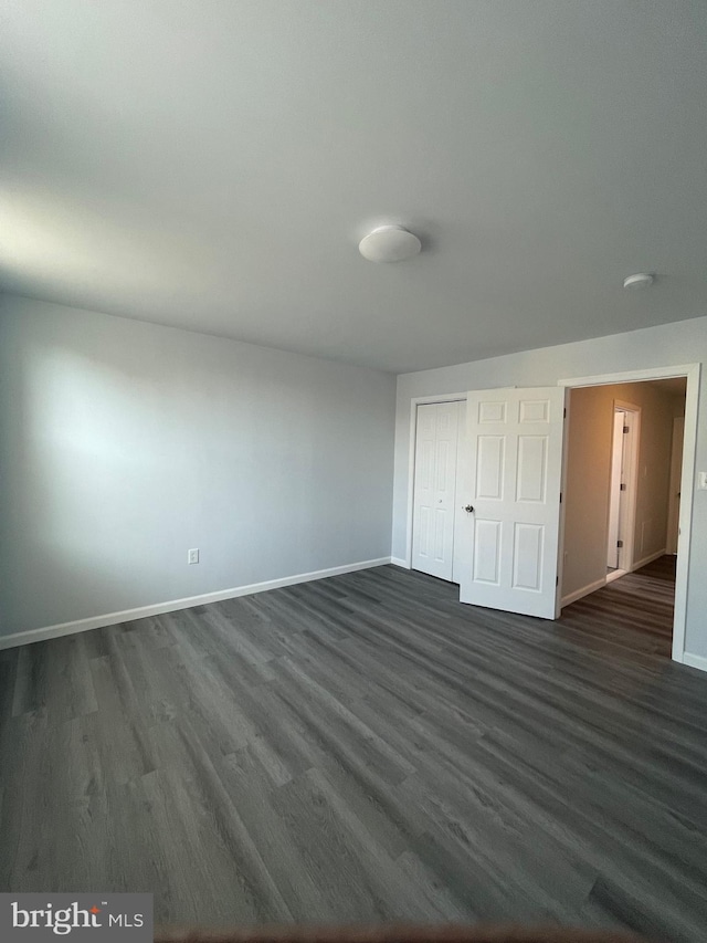 unfurnished bedroom with a closet, dark wood finished floors, and baseboards