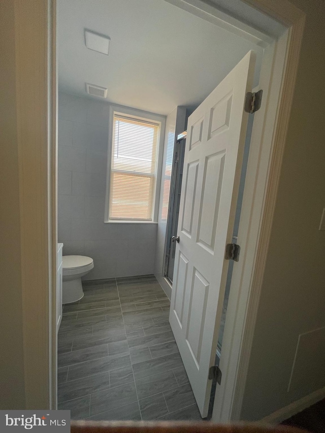 bathroom featuring tile walls, visible vents, a shower stall, and toilet