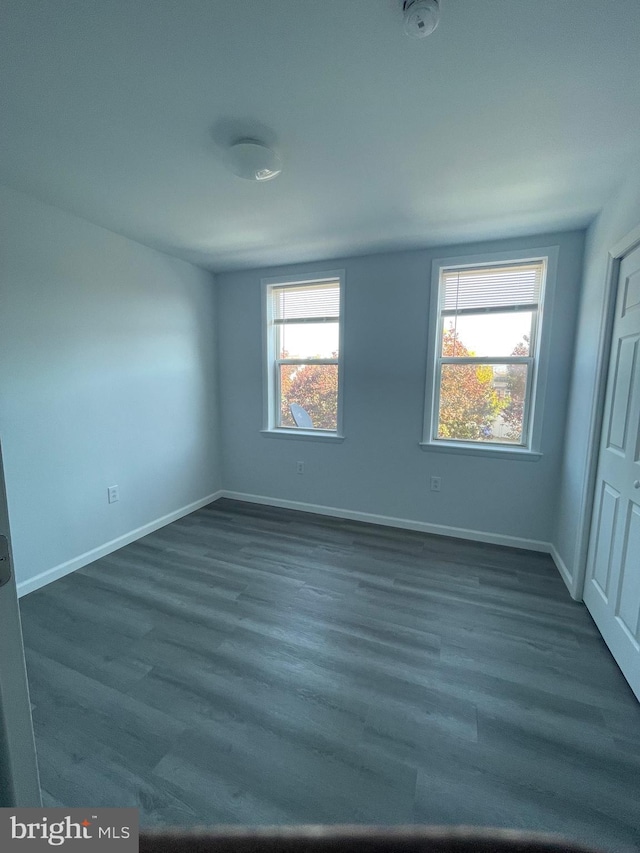 empty room with dark wood-type flooring and baseboards