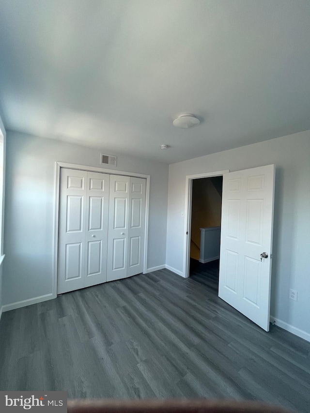 unfurnished bedroom with dark wood-type flooring, a closet, visible vents, and baseboards