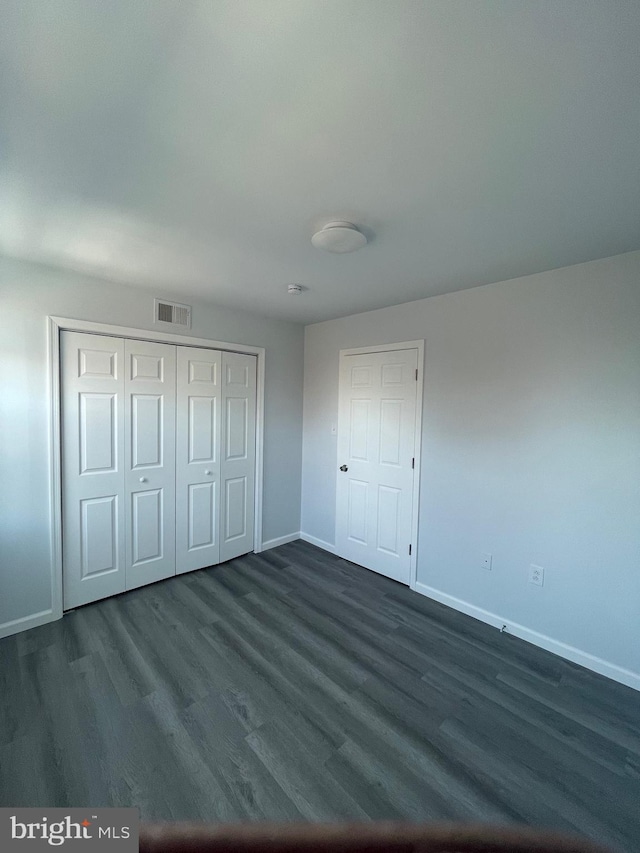 unfurnished bedroom featuring a closet, dark wood finished floors, visible vents, and baseboards