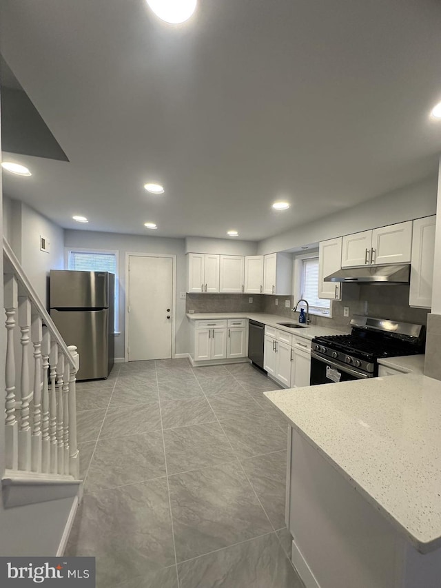 kitchen with backsplash, appliances with stainless steel finishes, white cabinetry, a sink, and under cabinet range hood