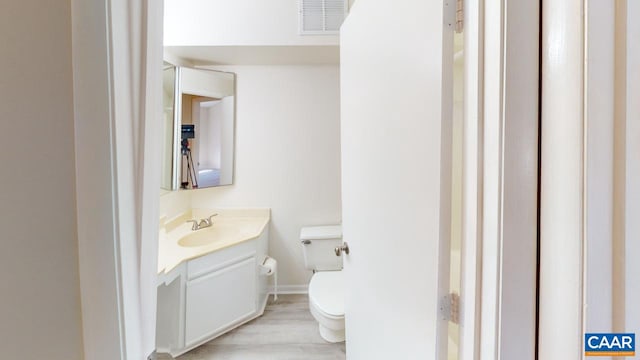 bathroom with toilet, visible vents, wood finished floors, and vanity