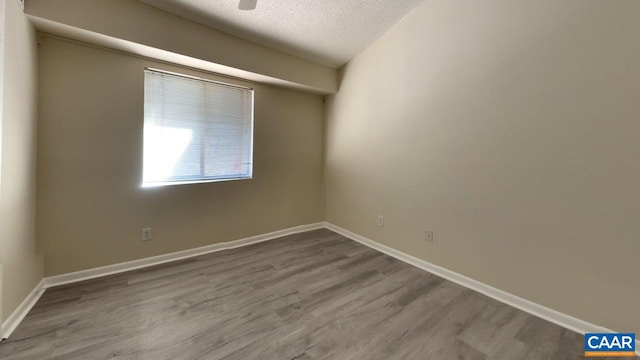 spare room with a textured ceiling, wood finished floors, and baseboards