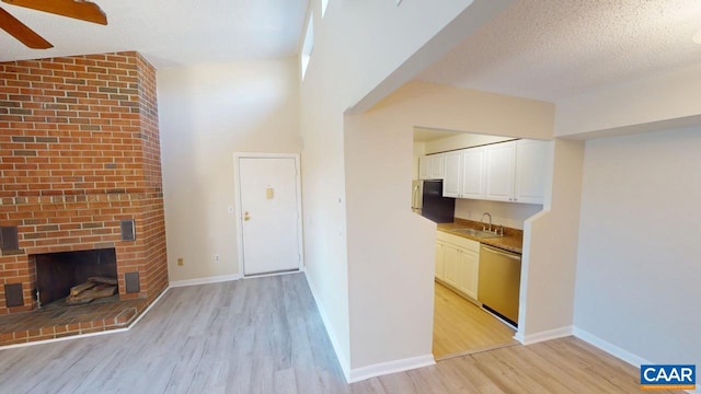 kitchen with light wood-style flooring, a sink, white cabinetry, stainless steel dishwasher, and a brick fireplace