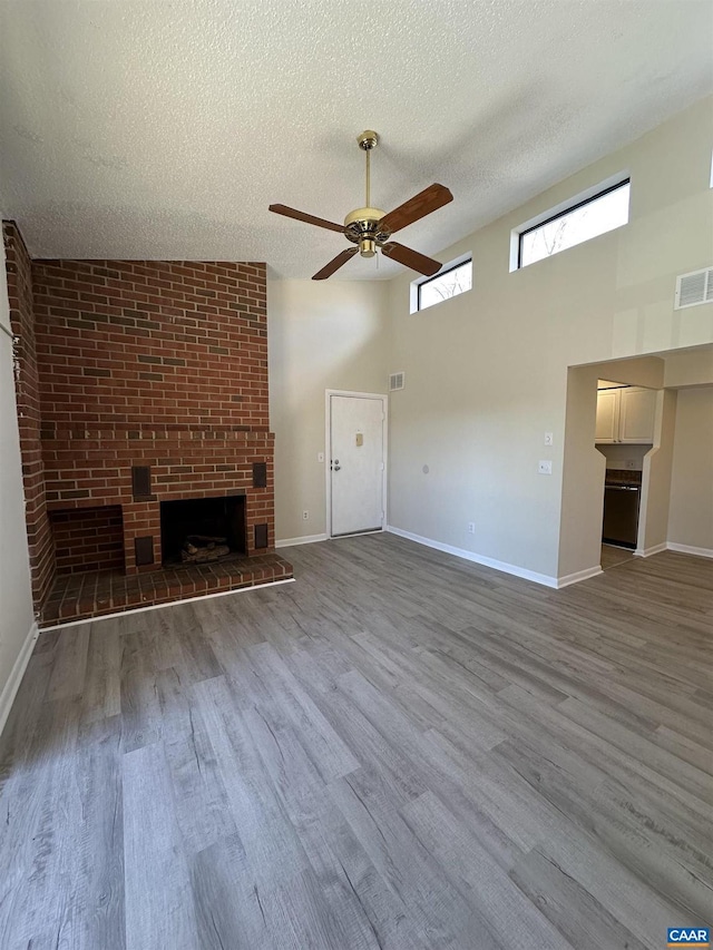 unfurnished living room featuring a textured ceiling, a brick fireplace, wood finished floors, and visible vents