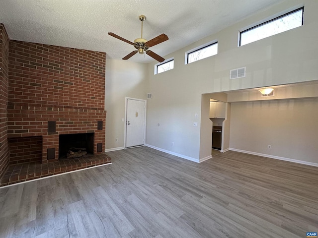 unfurnished living room with a textured ceiling, a brick fireplace, wood finished floors, and visible vents