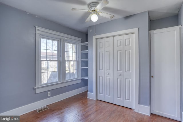 unfurnished bedroom with a closet, visible vents, baseboards, and wood finished floors