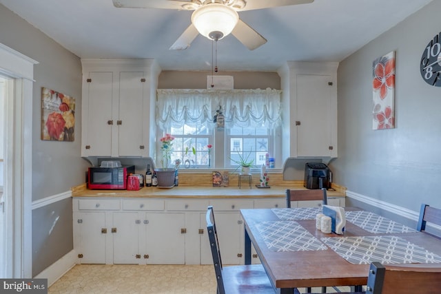 kitchen with a ceiling fan, light countertops, white cabinetry, and baseboards