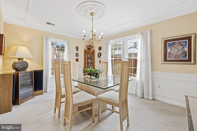 dining space with a wainscoted wall, visible vents, ornamental molding, light carpet, and a chandelier