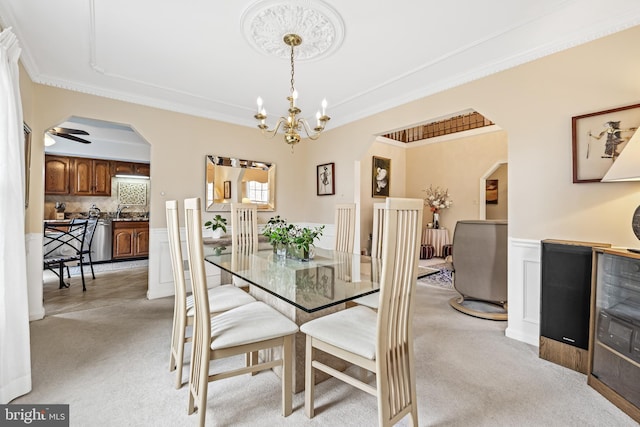 dining room featuring a wainscoted wall, arched walkways, ornamental molding, and light colored carpet