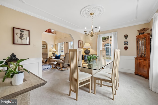 dining area featuring arched walkways, a healthy amount of sunlight, a wainscoted wall, and light colored carpet